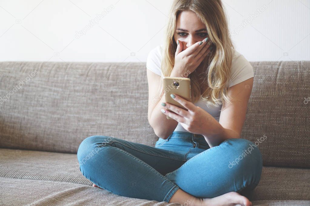 Shocked young woman looking at smartphone screen seeing something unbelievable