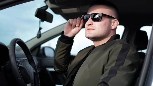 A magabiztos fiatal stílusos férfi napszemüveg a kocsijában oldalnézete — Stock Fotó