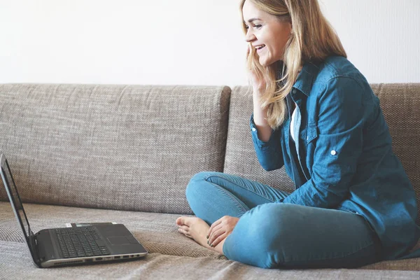 Rubia sonriente relajándose en el sofá con su portátil en casa en la sala de estar — Foto de Stock