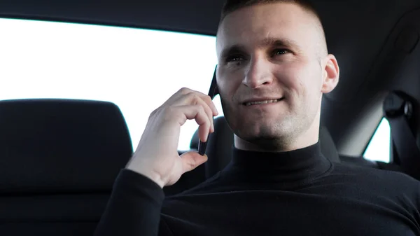 Fiatal üzletember beszél mobiltelefonon ülve a hátsó ülésen egy autó — Stock Fotó