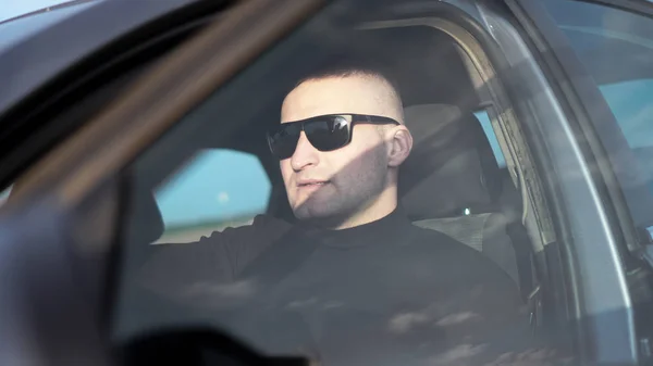 Vista lateral de confiante jovem homem elegante em óculos de sol em seu carro — Fotografia de Stock
