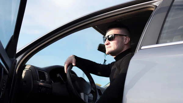 A magabiztos fiatal stílusos férfi napszemüveg a kocsijában oldalnézete — Stock Fotó