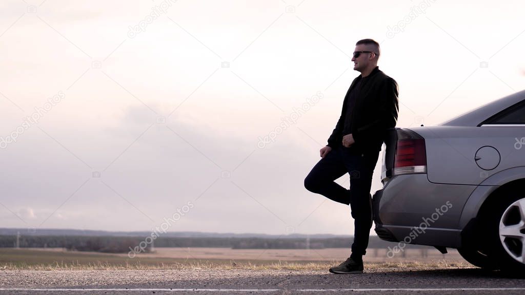 Sde view of businessman in eyeglasses sitting on car trunk at nature background