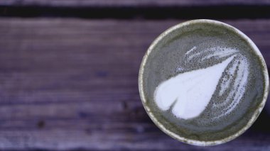 Ahşap üzerinde latte sanatı ile Matcha çayı fincan bulanık arka plan, metin için yer.