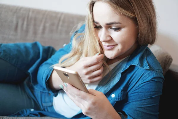 Ritratto di donna pensierosa sognante sdraiata sul divano con smart phone in mano — Foto Stock