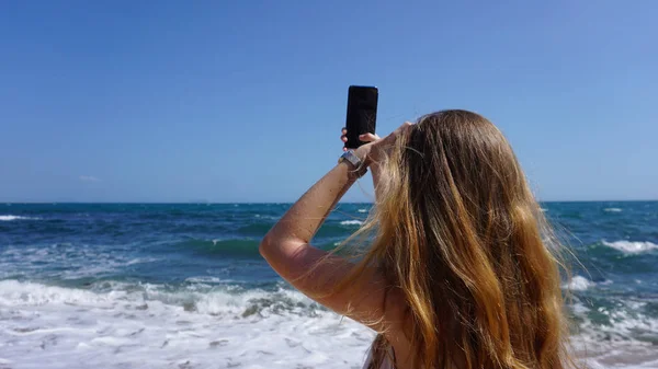 Крупный план женщины с помощью мобильного телефона, пляжа и моря на заднем плане — стоковое фото