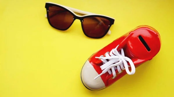 Caja de dinero en forma de zapatillas. Gafas de sol sobre fondo amarillo — Foto de Stock