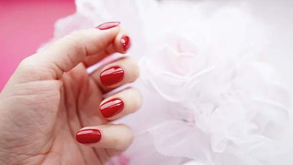 มือผู้หญิงที่สวยงามด้วยเล็บสีแดงกับพื้นหลังของช่อดอกไม้แต่งงาน — ภาพถ่ายสต็อก