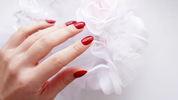 Bela mão feminina com unhas vermelhas no fundo de um buquê de casamento — Fotografia de Stock