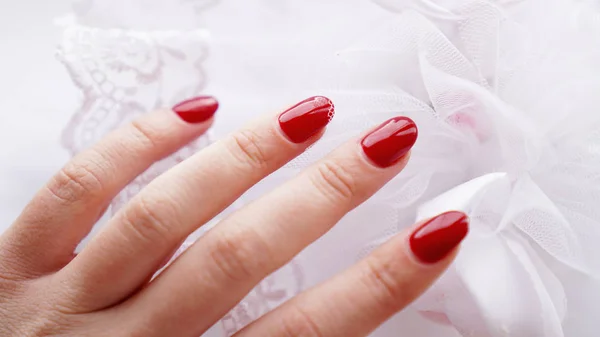 Bela mão feminina com unhas vermelhas no fundo de um buquê de casamento — Fotografia de Stock