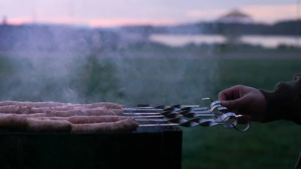 Grilling sausages at sunset outdoors gathering with friends and family — Stock Photo, Image