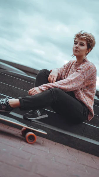 Uma menina bonita segurando um skate enquanto sentado no parque de skate — Fotografia de Stock