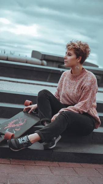 Une belle jeune fille tenant un skateboard assis dans un skatepark — Photo