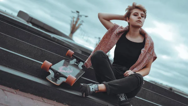 Uma menina bonita segurando um skate enquanto sentado no parque de skate — Fotografia de Stock