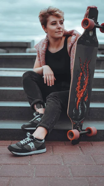 Krásná mladá dívka, která drží skateboard, zatímco sedí na skateparku — Stock fotografie