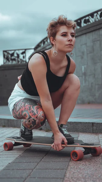 Beautiful young girl with tattoos sits on longboard