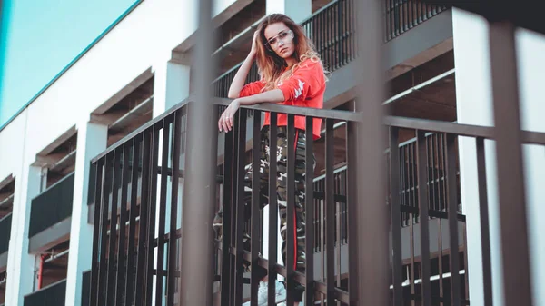 Modelo de moda con capucha roja con inscripción Los Ángeles posando en el aparcamiento —  Fotos de Stock