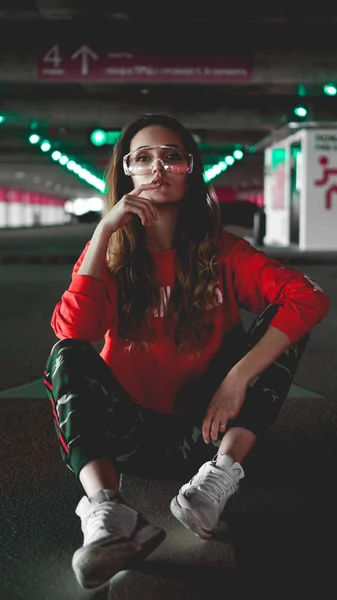 Pretty young woman sitting on car parking. Wearing stylish urban outfit — Stock Photo, Image