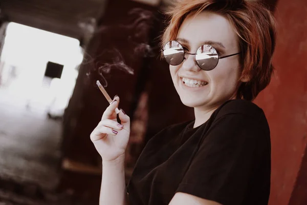 Menina milenar com cabelo vermelho curto e óculos de sol espelho fumar cigarro — Fotografia de Stock