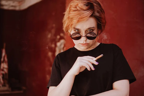 Тисячолітня дівчина з коротким рудим волоссям і дзеркальними сонцезахисними окулярами для куріння сигарети — стокове фото