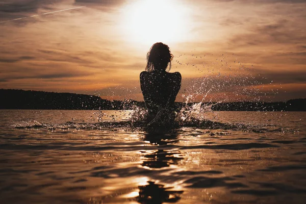 Молодая модель купается в море - время захода солнца. Привлекательный силуэт с брызгами — стоковое фото