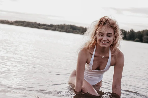 Vacker sexig kvinna i en vit baddräkt med en öppen rygg poserar nära sjön, — Stockfoto