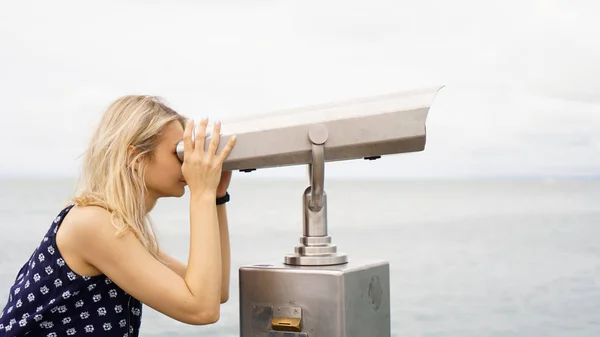 Woman standing on cruise liner deck and looking in binocular, half body