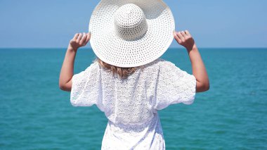 kum deniz kenarında üzerinde duran ve şapka tutan genç bir kadın