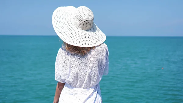 Молодая женщина, стоящая на песке у моря и держащая шляпу — стоковое фото