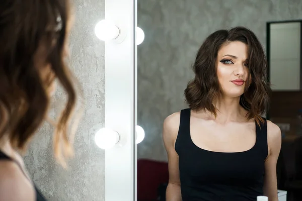 Porträtt av elegant kvinna med lockigt hår tittar på reflektion i spegeln — Stockfoto