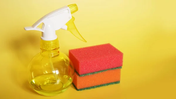 Cleaning products on yellow background including spay cleaner and a sponges