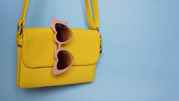 Yellow bag and heart-shaped sunglasses on blue background