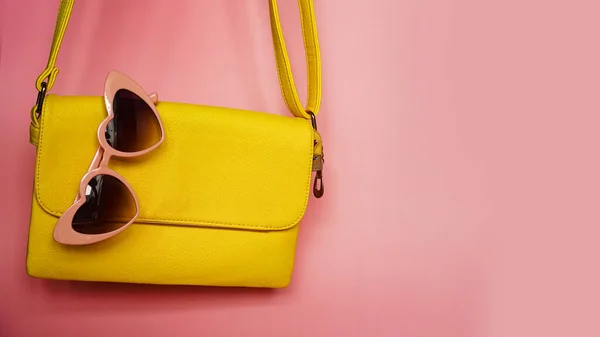Yellow bag and heart-shaped sunglasses on pink background — Stock Photo, Image
