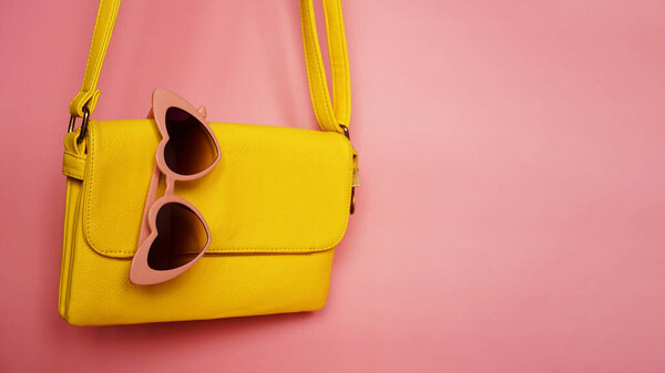 Yellow bag and heart-shaped sunglasses on pink background