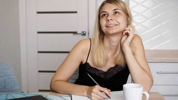 A woman sits in kitchen and writes a letter or her wishes — Stock Photo, Image