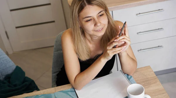 Una mujer se sienta en la cocina y escribe una carta o sus deseos — Foto de Stock