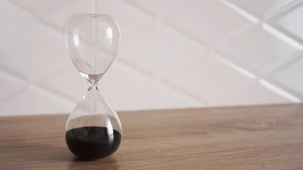 Reloj de arena cristal con arena negra sobre mesa de madera — Foto de Stock