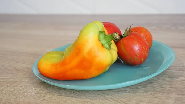 Tomate e pimenta em uma placa azul em um fundo leve na cozinha — Fotografia de Stock