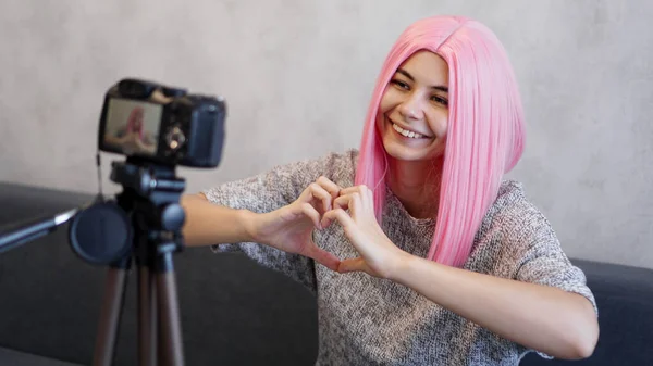 La donna guarda la telecamera e mostra il segno della forma del cuore. Ragazza con i capelli rosa — Foto Stock