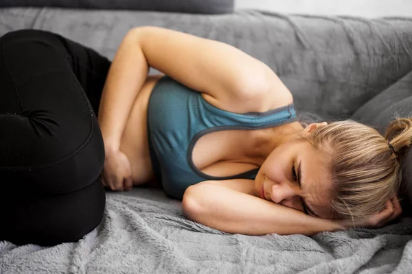 Vista lateral de la mujer que sufre de dolor de estómago acostado en el sofá en casa — Foto de Stock