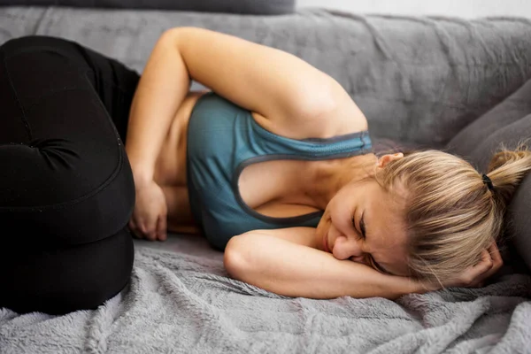 妇女肚子痛躺在家里沙发上的侧视图 — 图库照片