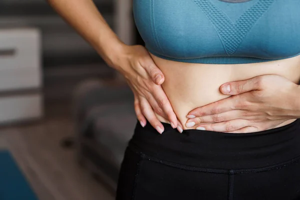 Close up of the woman holding her belly. Pain after home workout.