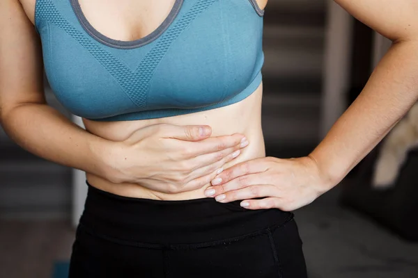 Close up of the woman holding her belly. Pain after home workout.