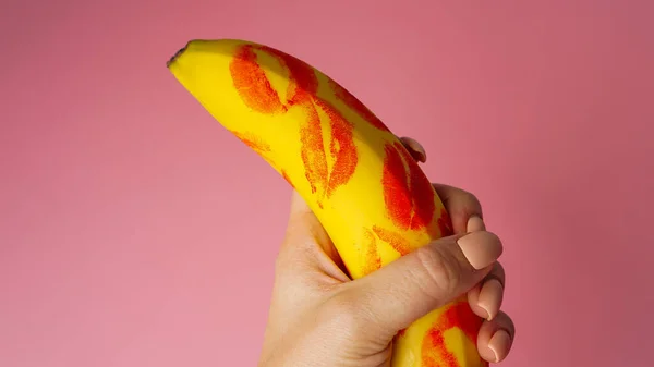 Nő kéz gazdaság banán piros rúzs jelölések rózsaszín háttér — Stock Fotó
