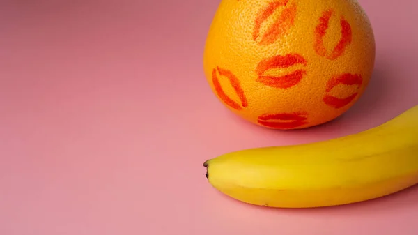 Banan och grapefrukt med spår av rött läppstift på rosa bakgrund — Stockfoto