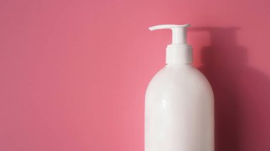 Açık pembe arka planda beyaz bir antiseptik pompa şişesi.