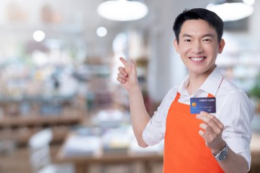 Genç zeki, çekici Asyalı erkek restoran sahibi el işareti. Kredi kartı online satın alma siparişi. Ev konseptinden Asya önlüğü üniforması.