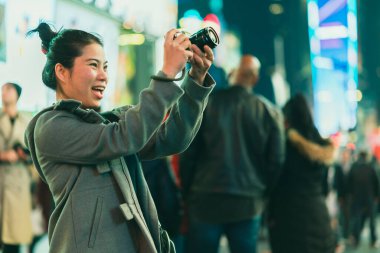 Asyalı kadın gezgin gülümseme, mutluluk, aynasız kamera, gece hayatı turnesinin keyfini çıkar. Kış mevsiminde arka planda bulanık insanlar olur.