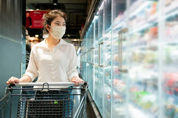 new normal after covid epidemic young smart asian female shopping new lifestyle in supermarket with face shild or mask protection hand choose fresh vegetable of fruit new normal lifestyle