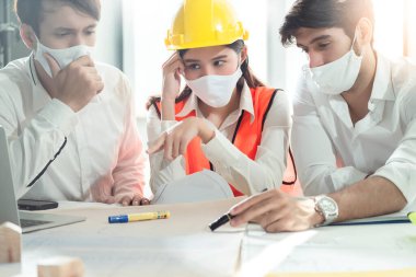 Kafkasyalı erkek ve Asyalı kadın mühendisler, Corona virüsü salgınında enfeksiyon yayılmış sosyal mesafe buluşmasının maskesinin korunmasıyla ciddi bir toplantı yapıyorlar.